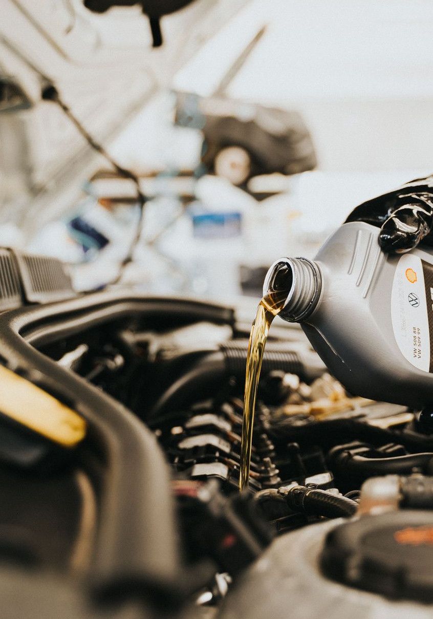 Close-up of a mechanic pouring engine oil into a car engine in an auto repair shop.